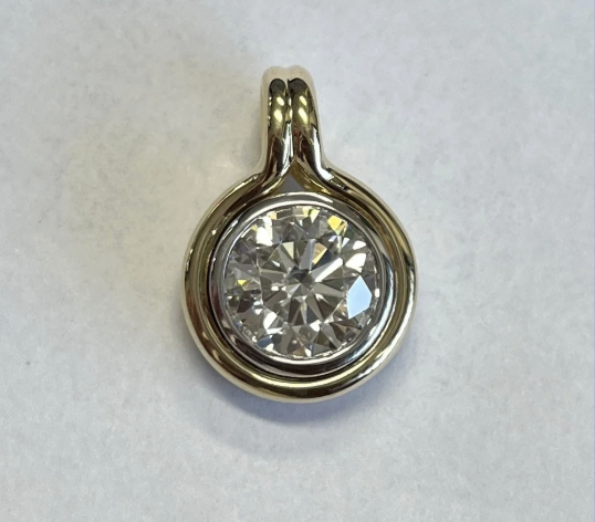 A close-up of the Lab Grown Round Diamond Bezel Charm, featuring a round lab grown diamond in a smooth gold bezel setting by Janet Heller Fine Jewelry, photographed on a plain white background.