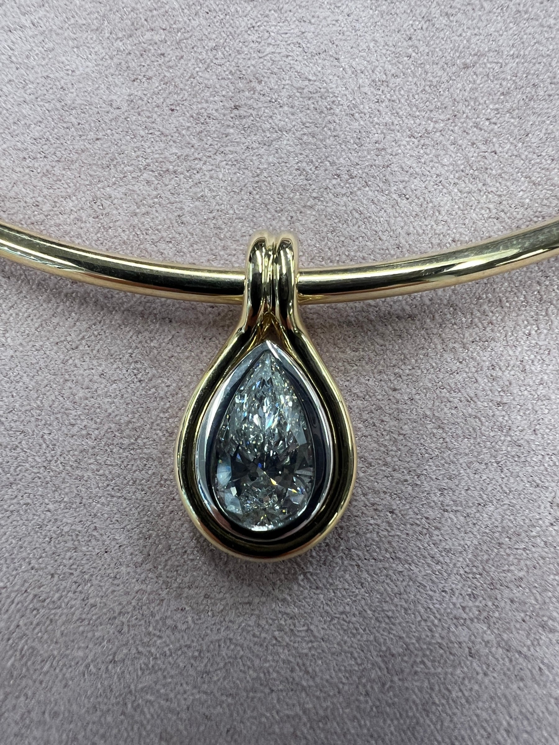 The Two Tone Pear Lab Diamond Charm necklace features a pear-shaped lab diamond set in a two-tone bezel, showcased against a soft, light beige background.
