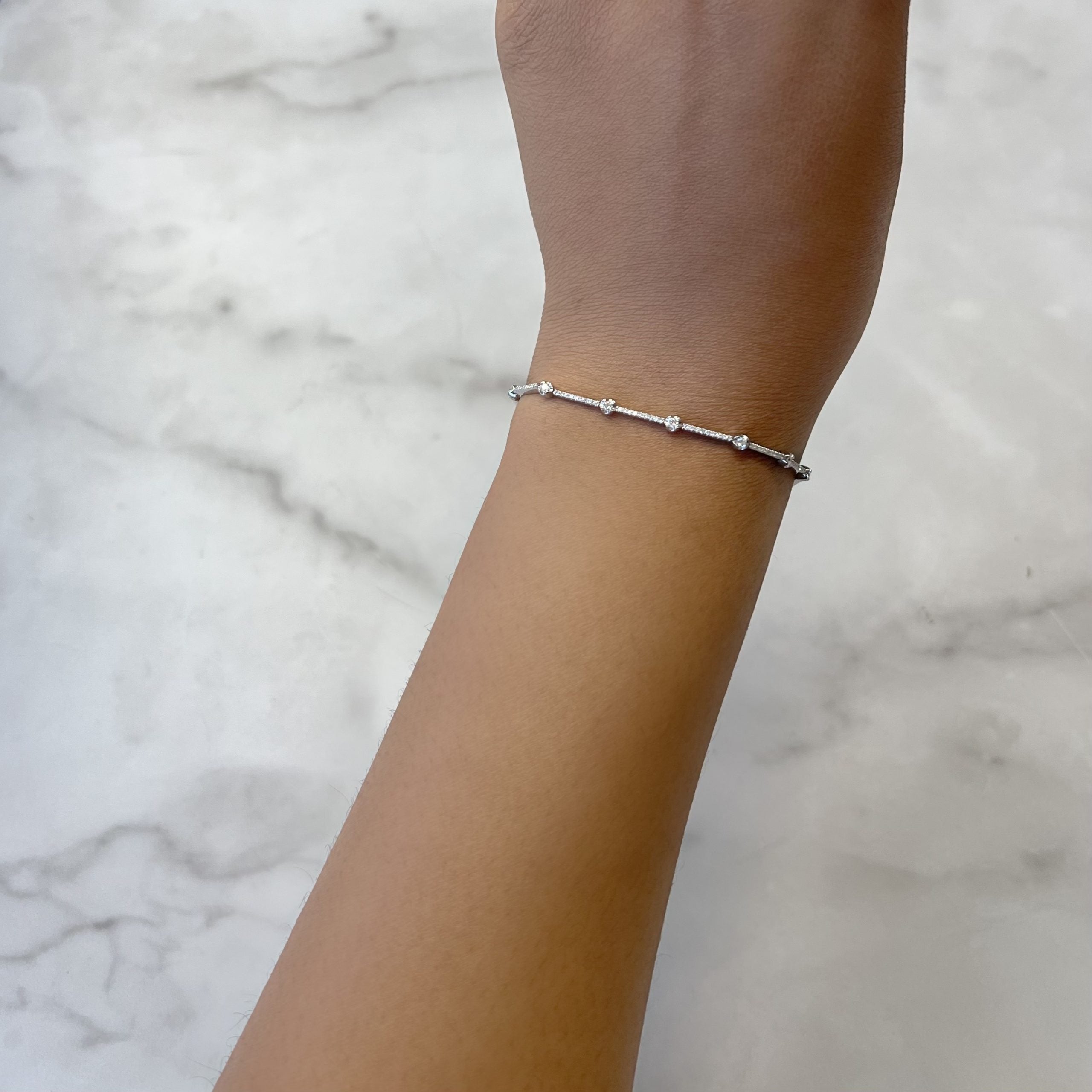 A hand adorned with the Segmented Diamond Bracelet from Janet Heller Fine Jewelry, featuring delicate silver beads and sparkling diamonds, rests on a light marble surface—an elegant choice for custom jewelry requests or other inquiries.