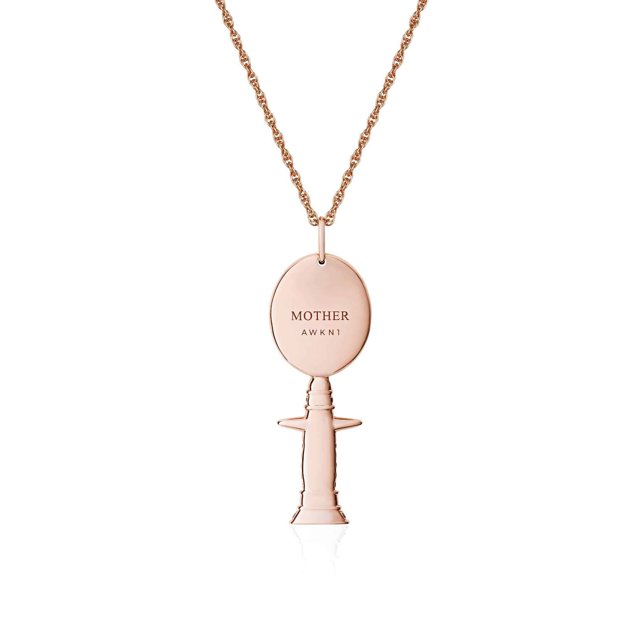 A rose gold Brown Mother Moon Goddess Necklace with an oval pendant engraved with MOTHER AWKNI, paired with a small, stylized pacifier charm. Both elements are joined together and suspended from a twisted rope chain.