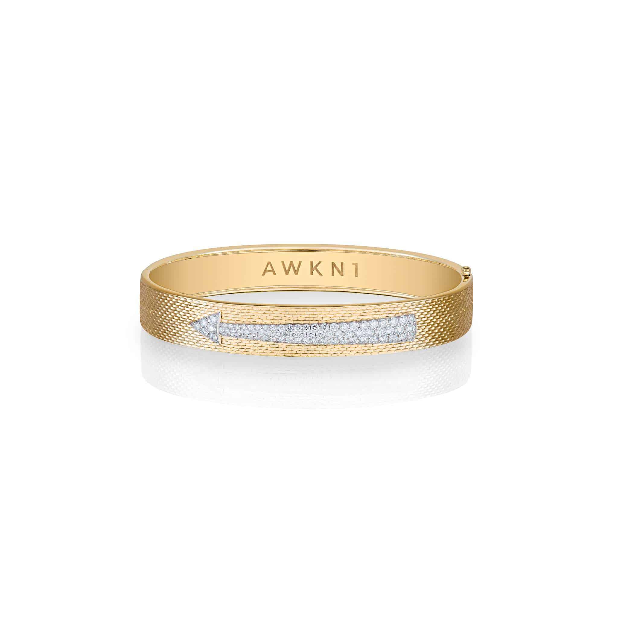 Introducing the Diamond Arrow Bangle—a gold bangle bracelet with a textured band, adorned with a row of sparkling white diamonds in the shape of an arrow and an AWKN1 engraving on the inner side.