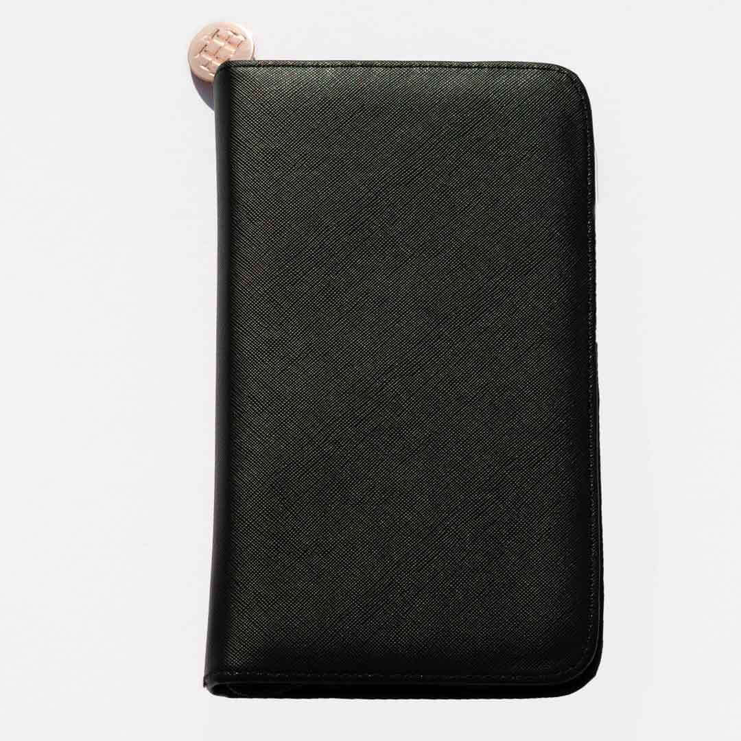 A black Travel Case crafted from vegan leather with a textured surface and a round metallic zipper pull, lying on a white background.