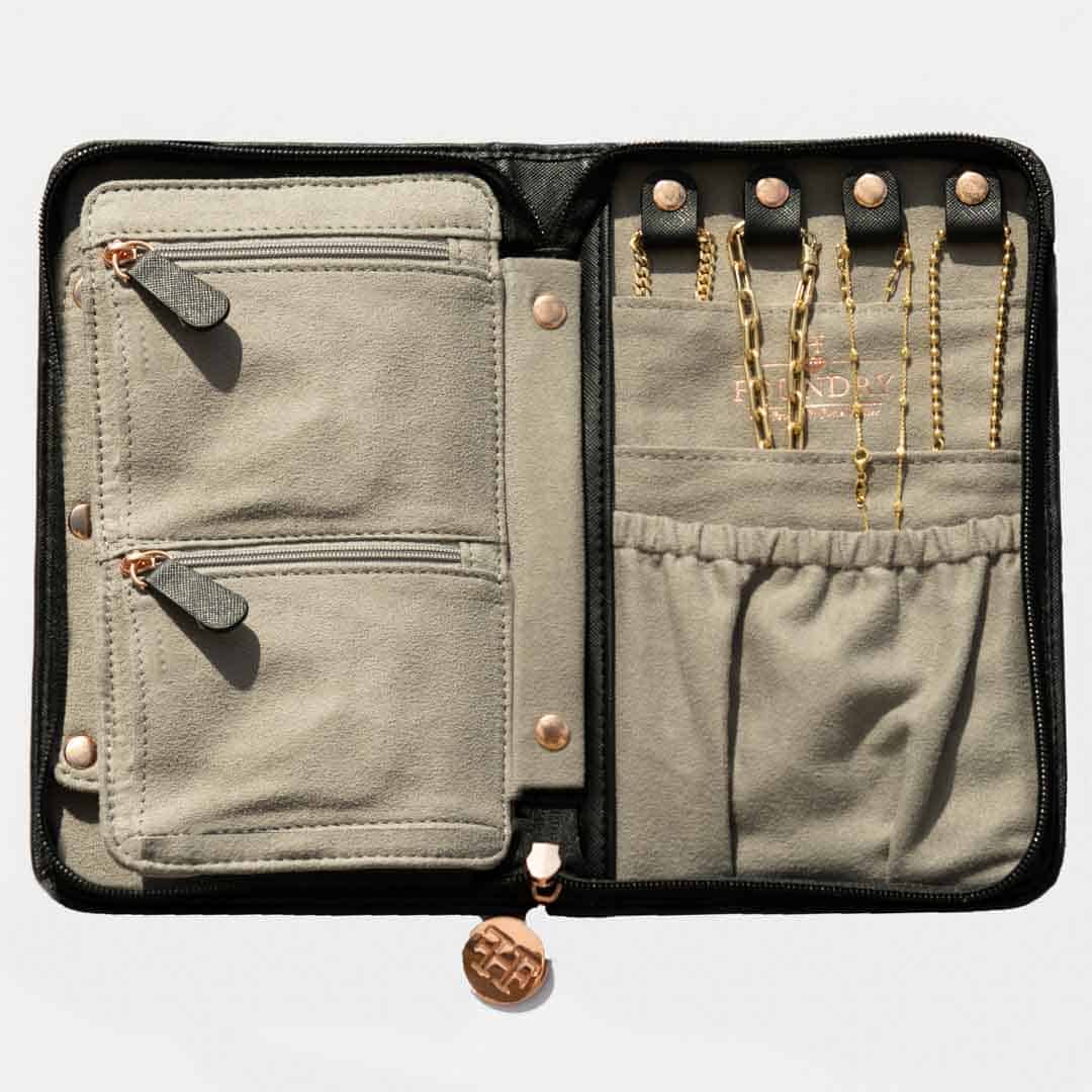 The Travel Case features a vegan leather exterior, a beige suede interior, two zippered pockets, an elastic pouch, four snap loops for holding gold chains, and a round zipper pull.